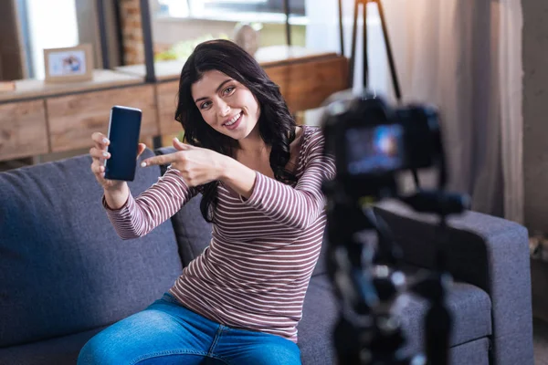 Deliziosa donna felice che indica il suo telefono — Foto Stock