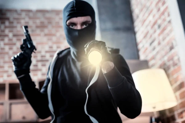 Wütender maskierter Räuber mit Taschenlampe und Waffe — Stockfoto