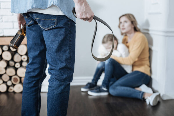 Злой и пьяный папочка держит бутылку и ремень
