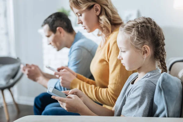 Niña seria y sus padres usando teléfonos — Foto de Stock