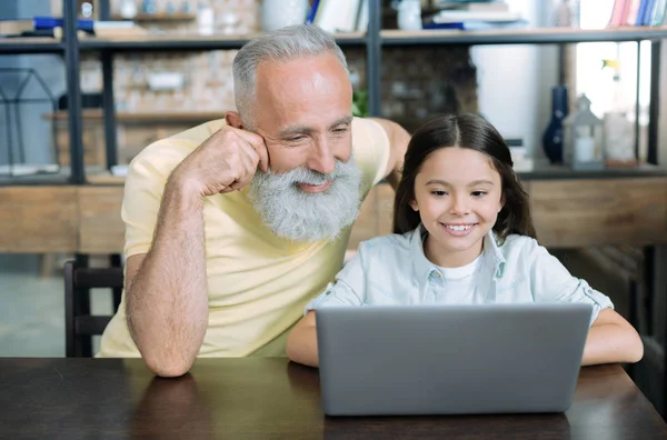 Amando abuelo mirando a chica trabajando en portátil — Foto de Stock