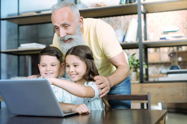 Alegre abuelo usando portátil con sus nietos — Foto de Stock