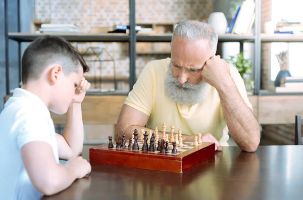 Hombre mayor pensativo y su nieto jugando ajedrez — Foto de Stock