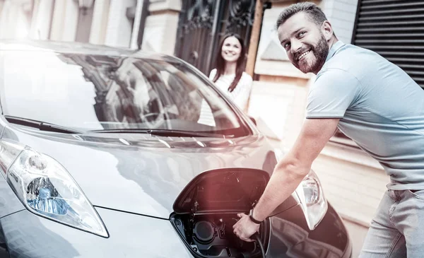 Hombre de mente positiva sonriendo mientras carga su coche respetuoso con el medio ambiente —  Fotos de Stock