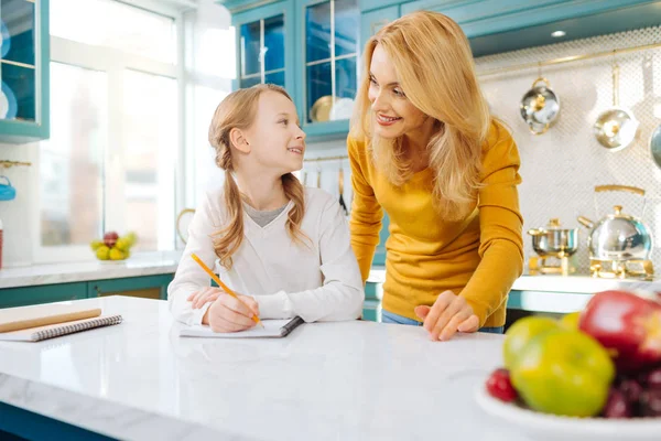 Cheerful girl looking at her mother and holding a pencil — Stock Photo, Image