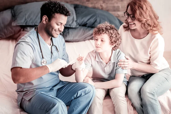 Medico sorridente bendaggio mano di giovane paziente — Foto Stock