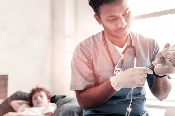 Concentrated doctor adjusting infusion bottle for teenager — Stock Photo, Image