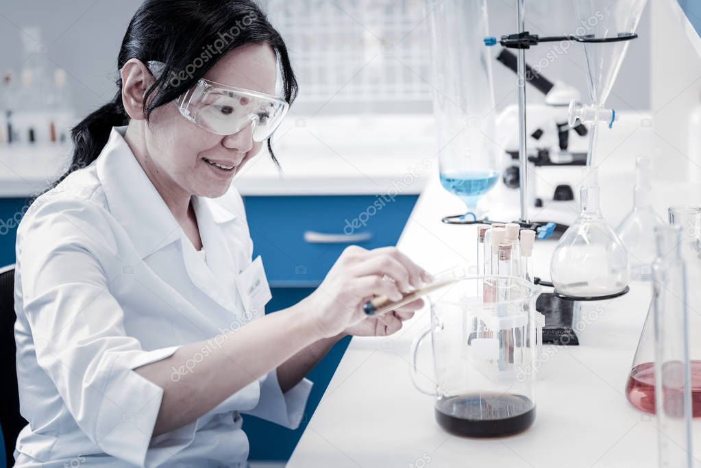 Cheerful lady pouring liquid into beaker in laboratory