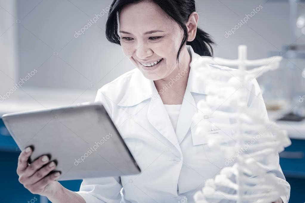 Satisfied female scientist smiling while looking at tablet computer