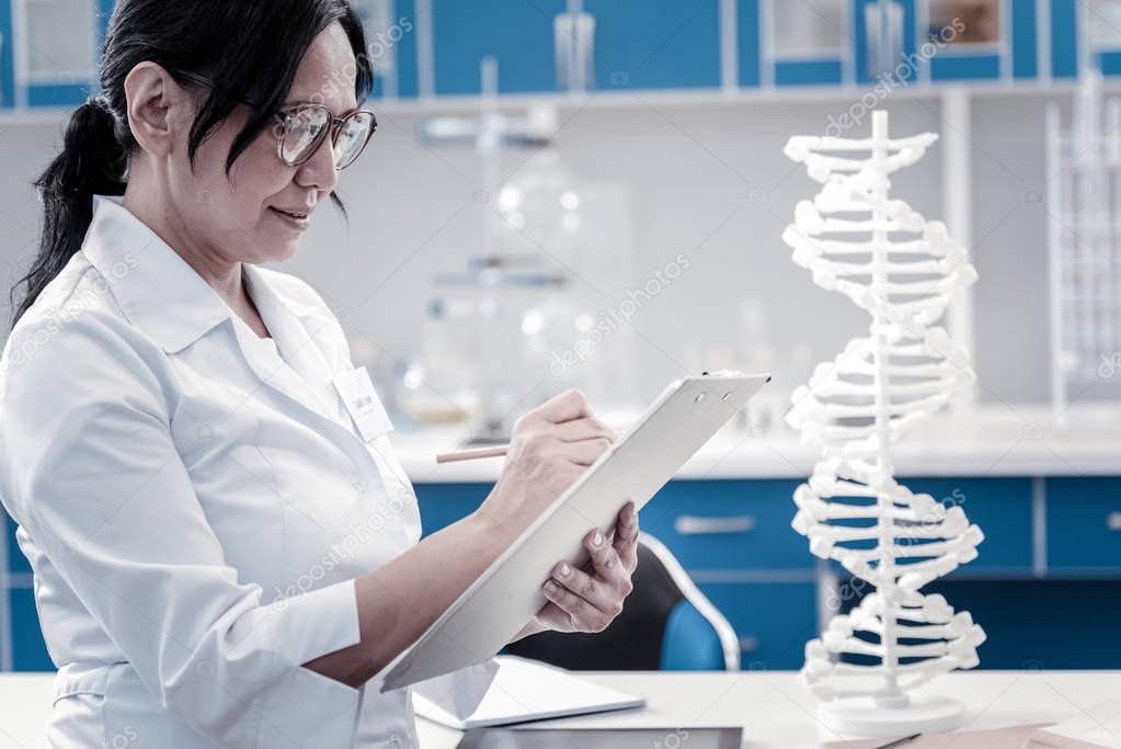 Concentrated mature lady writing something down in laboratory