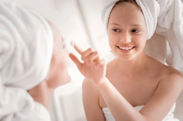 Deleitado chica positiva poniendo crema en su cara de madres —  Fotos de Stock