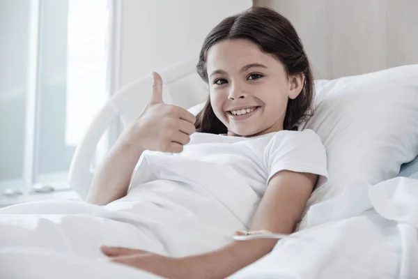 Brave little patient smiling and thumbing up in hospital bed — Stock Photo, Image