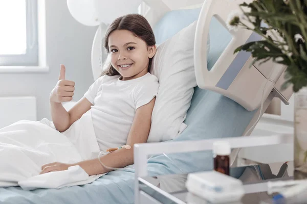 Charmerende barn opholder sig positivt, mens liggende i hospitalssengen - Stock-foto