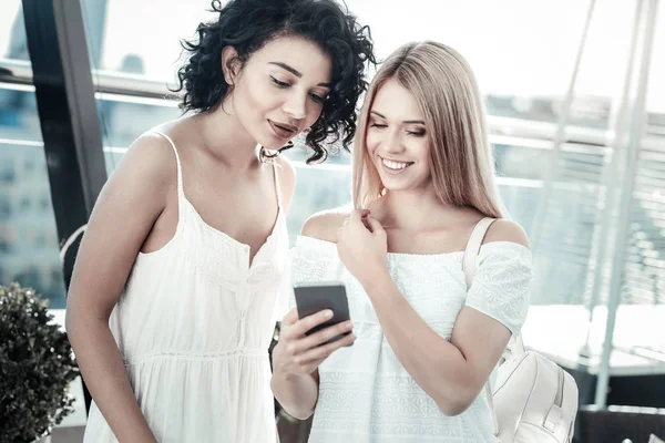 Mujer joven positiva mostrando su teléfono inteligente a su amigo —  Fotos de Stock