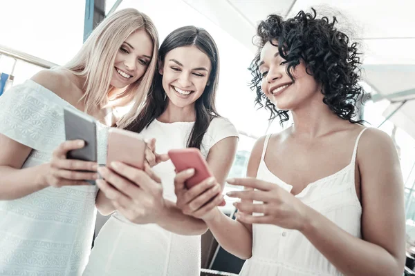Mujeres jóvenes felices mostrando sus teléfonos inteligentes el uno al otro —  Fotos de Stock