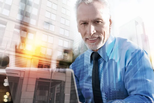 Positiver älterer Mann lächelt, während er mit einem Laptop sitzt — Stockfoto