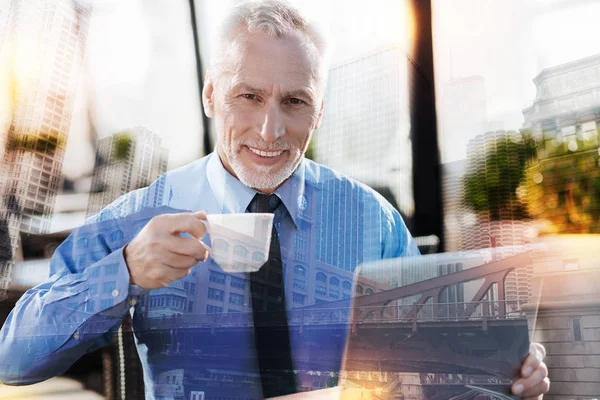 Aangenaam volwassen man koffie drinken en die op zijn laptop werkt — Stockfoto