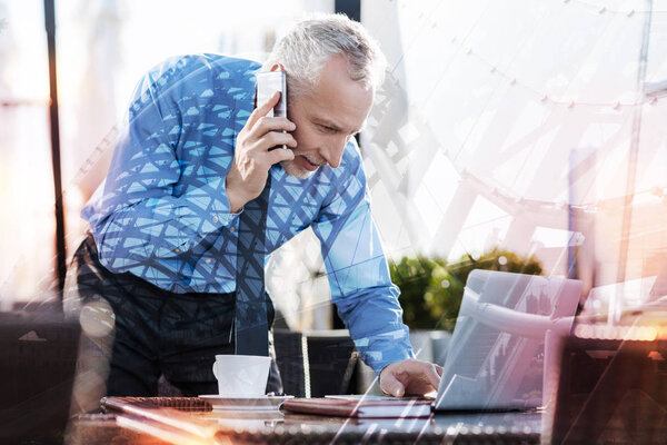 Clever employer having a phone talk while looking at his laptop