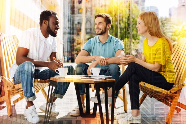 Tre amici seduti a tavola con tazze di caffè e chiacchiere — Foto Stock