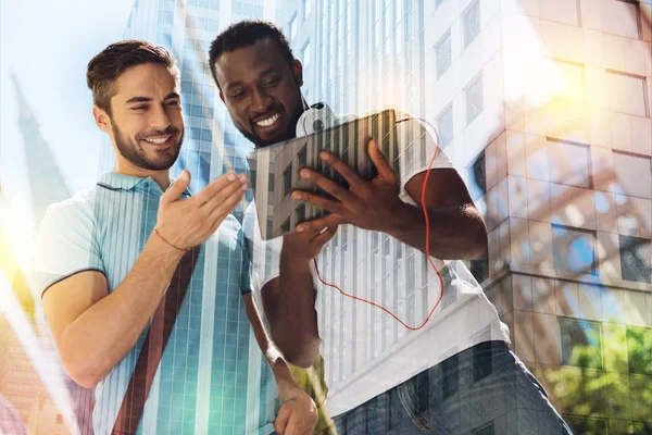 Lächelnder Student hält ein modernes Tablet in der Hand, während sein Freund es betrachtet — Stockfoto