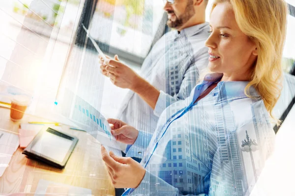 Jonge specialist glimlachen tijdens het kijken naar de statistieken in haar handen — Stockfoto