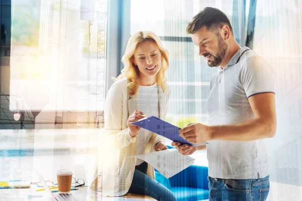 Mujer alegre sonriendo mientras mira las notas de su compañero de trabajo — Foto de Stock