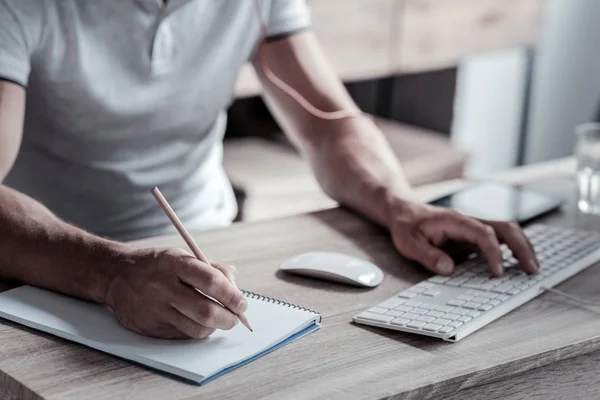 Close up of man taking notes while working on pc Stock Photo