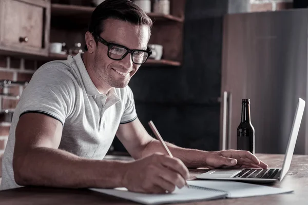 Joyful tusenåriga killen göra anteckningar medan du arbetar på laptop — Stockfoto