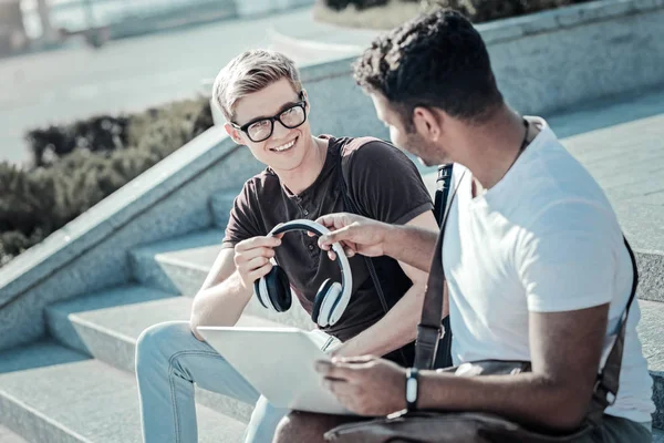 Netter junger Mann gibt seinem Freund Kopfhörer — Stockfoto