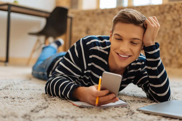 Exuberant young man lying on the floor with his phone — Stock Photo, Image