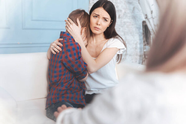 Worried mother calming her son in psychologist office