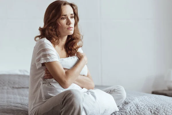 Depressive reife Frau umarmt Kissen, während sie auf dem Bett sitzt — Stockfoto