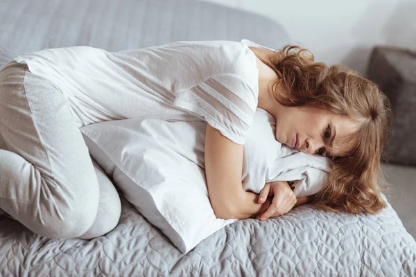 Λυπημένη γυναίκα ξαπλωμένη στο κρεβάτι και αγκαλιάζει το μαξιλάρι της — Φωτογραφία Αρχείου