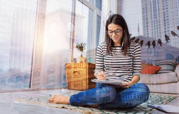 Mooie vrolijke student luisteren naar de muziek terwijl het doen van huiswerk — Stockfoto