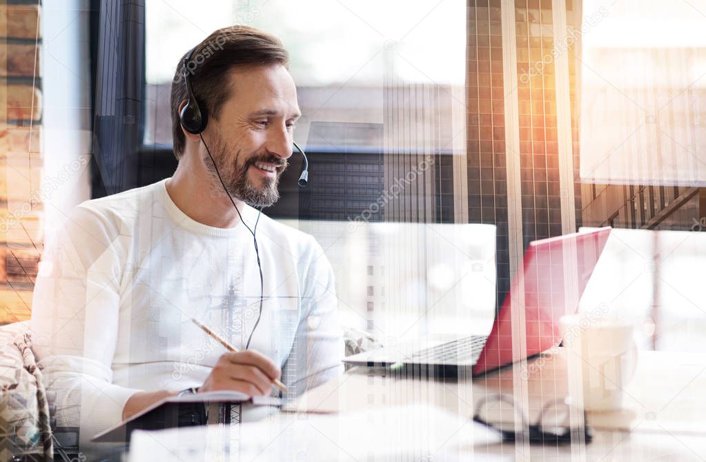 Cheerful young man participating in webinar and making notes