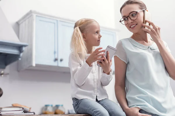 Encantadora chica sincera y madre usando teléfonos inteligentes —  Fotos de Stock