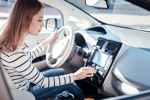 Mujer interesada ocupada sentada en el coche sosteniendo el panel de control táctil . — Foto de Stock
