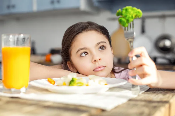 Ernstes Kind blickt auf das Gemüse auf ihrer Gabel — Stockfoto