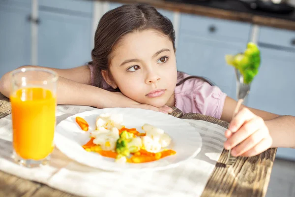 Unsmiling child looking at the vegetable on her fork — Stock Photo, Image