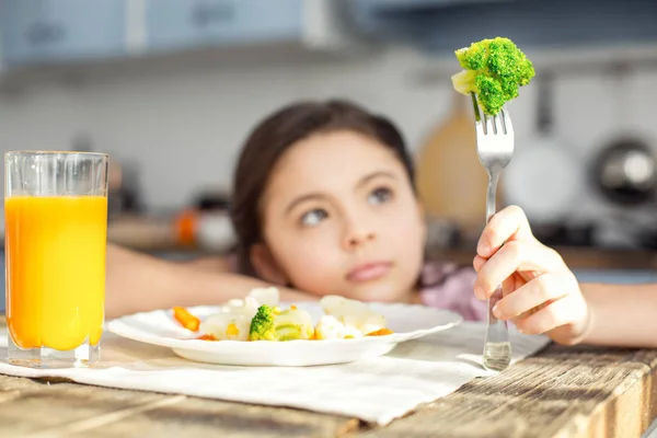 Criança atenciosa olhando para o vegetal em seu garfo — Fotografia de Stock