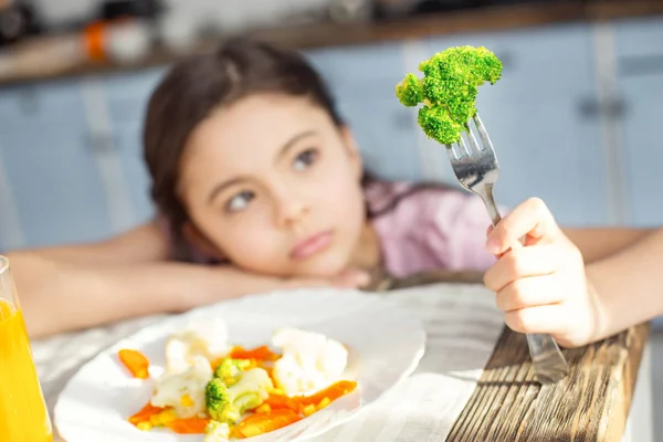 Sad girl looking at the vegetable on her fork — Stock Photo, Image