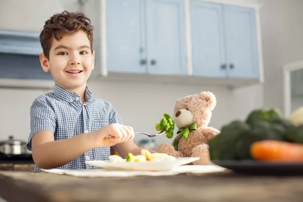 Menino feliz alimentando seu brinquedo com comida saudável — Fotografia de Stock
