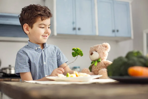 Smiling boy feeding his toy with healthy food — Stock Photo, Image