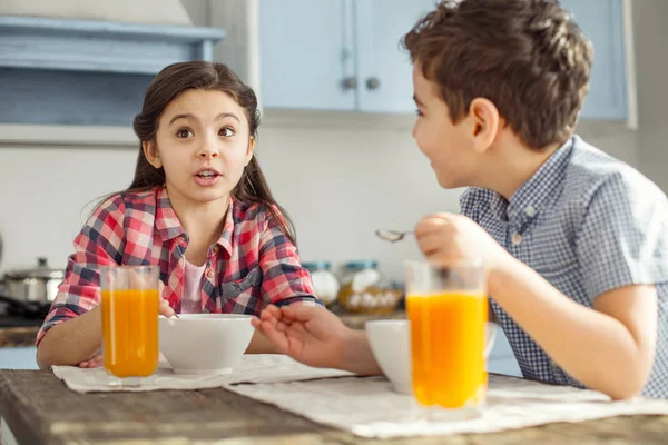 Fröhliches Mädchen, das mit ihrem Bruder spricht und isst — Stockfoto