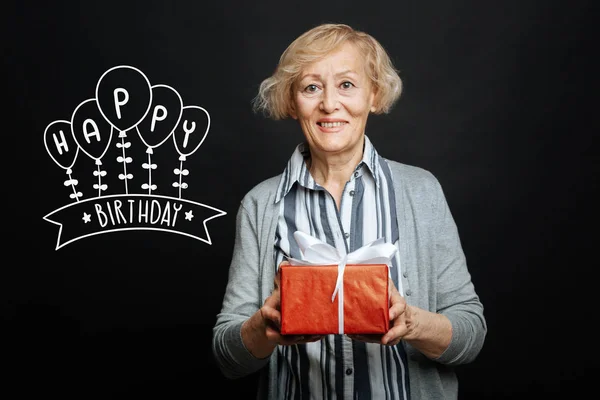 Alegre anciana sonriendo mientras sostiene un regalo de cumpleaños — Foto de Stock