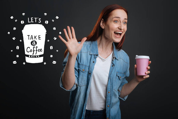 Excited woman waving her hand while holding a cup of coffee