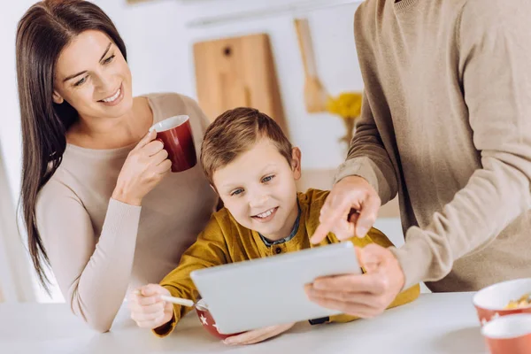 Pleasant parents showing video to son while he eating — Stock Photo, Image