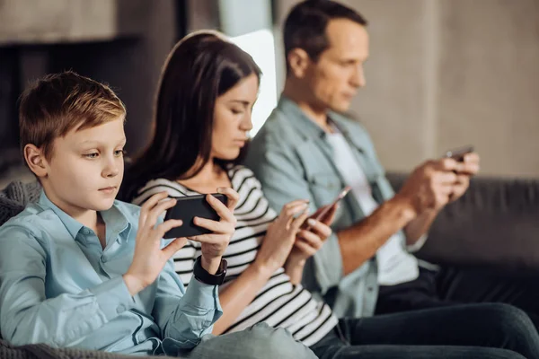 Мальчик и его родители пользуются телефонами — стоковое фото