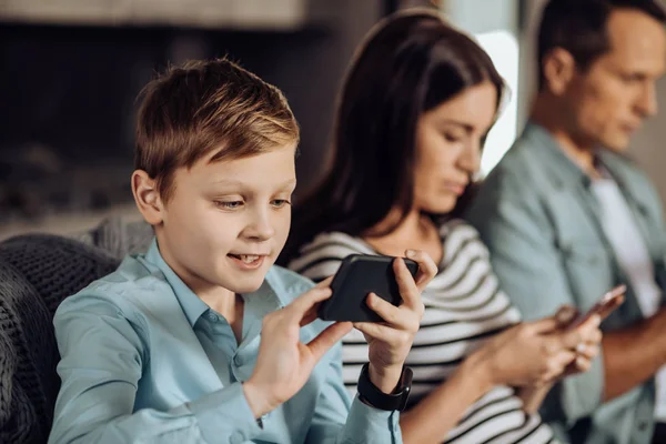 Мальчик-подросток играет по телефону рядом со своими родителями — стоковое фото