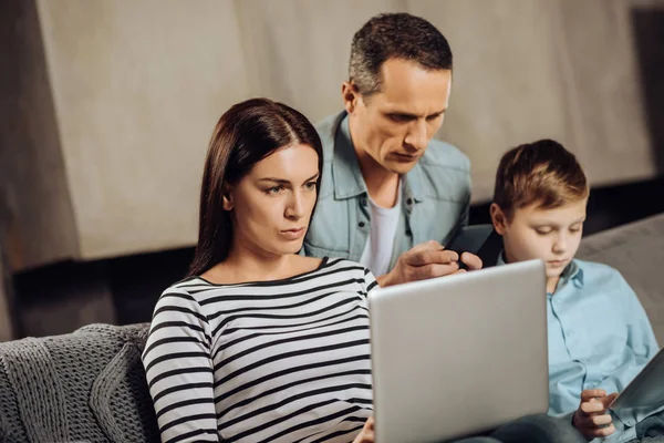 Молода жінка працює на ноутбуці, коли грає її сім'я — стокове фото